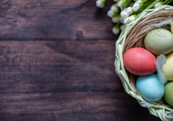 Colorful Easter eggs in a basket on the background of a wooden table, next to willow twigs and flowers.