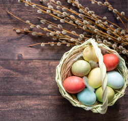 Colorful Easter eggs in a basket on the background of a wooden table, next to willow twigs and flowers.