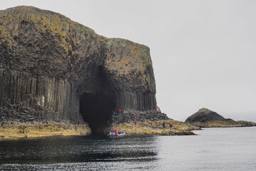 Tourists with boat visit Fingals Cave and hexagonal volcanic basalt rock columns, Isle of Staffa,...
