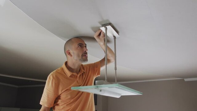A man unscrews the fixing of the ceiling lamp in the kitchen with a screwdriver to dismantle it.