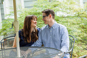 Acouple of a husband and wife sitting under a shaded umbrella patio table outside in the backyard