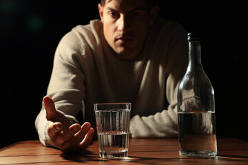 Addicted man with alcoholic drink at wooden table against black background, focus on glass