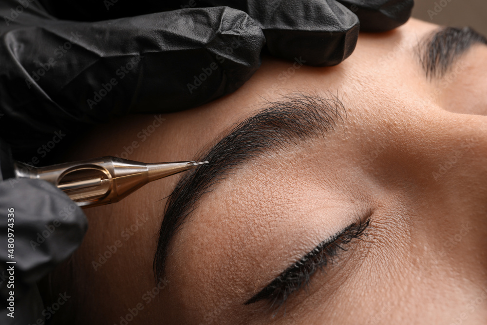 Wall mural Young woman undergoing procedure of permanent eyebrow makeup in tattoo salon, closeup