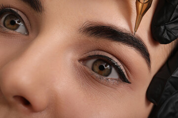 Young woman undergoing procedure of permanent eyebrow makeup in tattoo salon, closeup