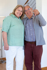 Pleased elderly couple showing keys at camera. Smiling family in glasses looking at camera after buying new home or apartment. Real estate, purchase concept