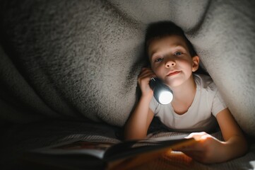 Child reading book in bed. Kids read at night. Little boy with fairy tale books in bedroom . Education for young children. Bedtime story in the evening. Cute kid under blanket in dark room with lamp.