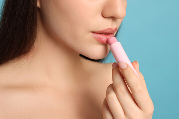Obraz na płótnie Canvas Young woman applying lip balm on turquoise background, closeup