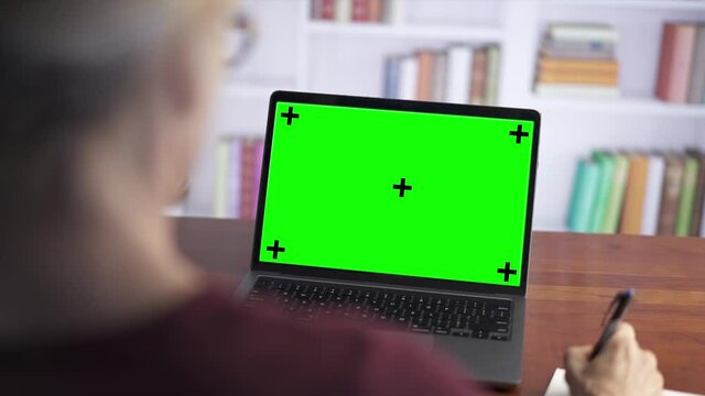 Over the shoulder shot of a business woman working looking at green screen. Office person using laptop computer with green screen.