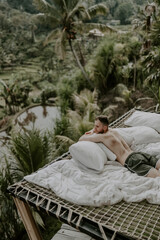 Young male traveller relaxing in a hotel in Bali, surrounded by nature, palm trees, rice fields and jungle views in Ubud, Indonesia, Asia