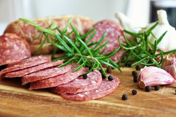 Traditional smoked salami sausages sliced with pepper, garlic and rosemary on wooden cutting board.