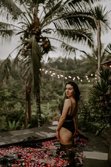 Fototapeta premium A young female traveller is relaxing by the small plunge pool of a jungle hotel in Bali surrounded by jungle, rice fields and tropical landscape