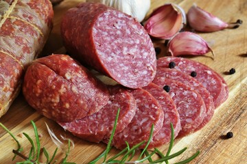 Traditional smoked salami sausages sliced with pepper, garlic and rosemary on wooden cutting board.