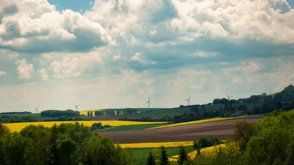 Electricity windmills under the cloudy evening sky at canola fields spring time
