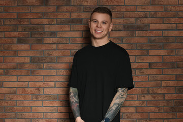 Smiling young man with tattoos near brick wall