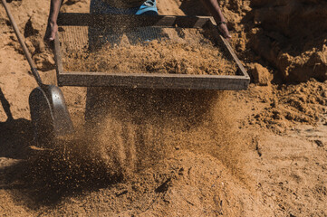 Worker of a brick factory strains sand with a shovel
 in a wheelbarrow, for the elaboration of bricks.