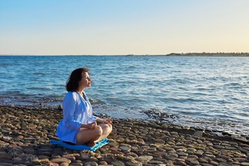 Mature woman sitting in lotus position meditating on the beach.
