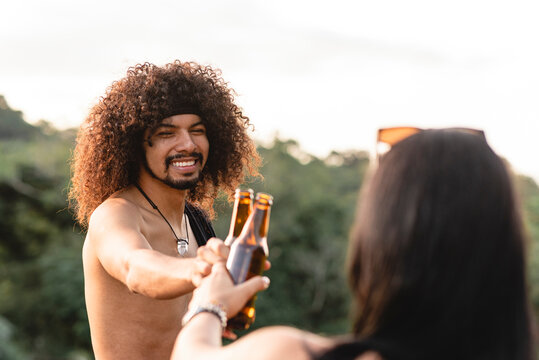 un hombre latino sonriente de cabello rizado brindando con cerveza con una mujer desconocida
