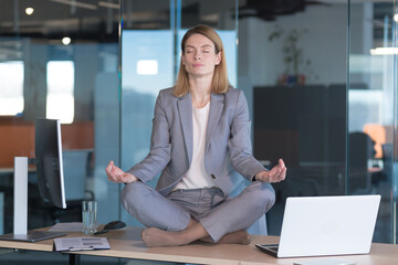 Business woman alone sitting at desk in her office, female employee meditating in lotus position