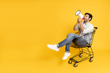 Young man sitting inside of shopping trolley and holding megaphone  isolated on yellow background, Announce concept - 480981587