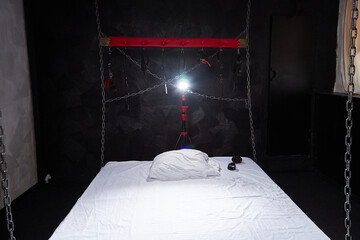 A bed with white linen and metal chains in the background. A room for BDSM sex