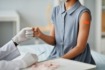 Close up of teenage African-American girl bumping fists with doctor after getting vaccinated against covid-19