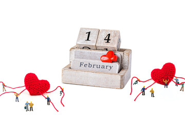Miniature people with wooden calendar 14 February and red heart shape  on white background.