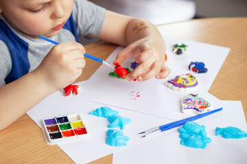 Cropped shot of a child coloring plaster figures with colored paints with a brush. Children's creativity, the creation of magnets