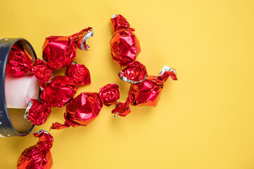 chocolates in red wrappers sticking out of their package. yellow background, valentines day.