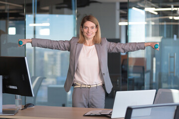 Beautiful and happy woman doing sports exercises in the office at work, during a break, business...