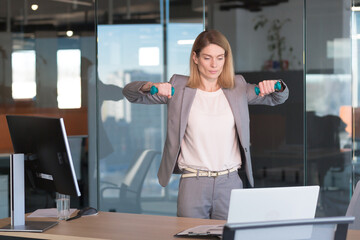 Beautiful and happy woman doing sports exercises in the office at work, during a break, business woman monitors health engaged in fitness