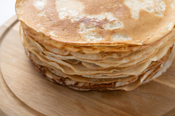 Shrovetide pancakes are stacked on the wooden plate. Thin pancakes with a crispy crust.  Pancakes for breakfast and Shrovetide.. Food background.