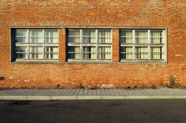 Brick wall with three large windows and curtains. Tiled concrete sidewalk and paved road in front. Background for copy space