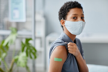 Portrait of teenage African-American girl showing shoulder with plaster after getting vaccinated against covid 19 in clinic