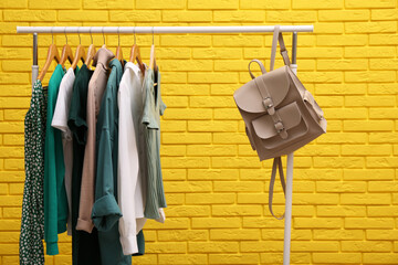 Rack with different stylish clothes and backpack near yellow brick wall