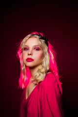 A girl in a pink dress and a silver crown in the backlight of pink neon. Fashion model for jewelry, bijouterie, silver earrings. Glitter makeup 80s 90s style