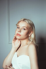 Naklejka premium Portrait of a bride, a woman in a white dress with a beautiful pink make-up. Long earrings as a decoration for a wedding, jewelry for the bride