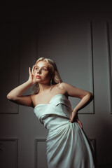 Dark fashion photo of a bride in a white dress. Gorgeous blonde looks at the camera in motion. Long beautiful earrings. Salon of wedding dresses.