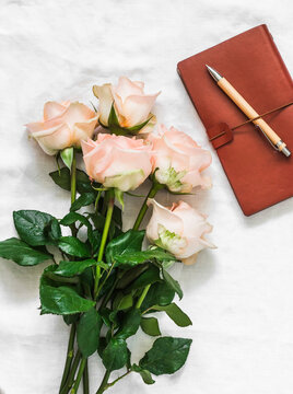 Delicate bouquet of roses, leather planner and pen on the bed on a light background, top view