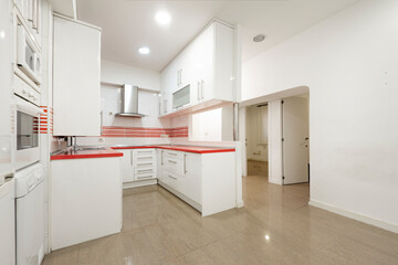 Large kitchen with white cabinets and red countertops with brick walls and reddish granite floors