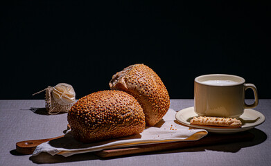 delicioso lanche com pão integral com gergelim sobre um guardanapo e uma xícara com pires de porcelana cheia de leite