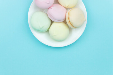 Colorful mini marshmallows looks like macaroons in a black plates on a blue pastel background. Food background.