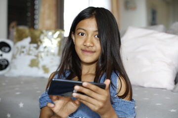 Une jeune fille asiatique sourit en utilisant son smartphone