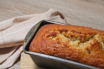 Freshly baked banana bread in baking tin on wooden board