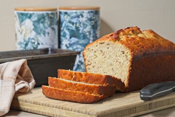 Freshly baked banana bread, sliced. on a wooden board with knife