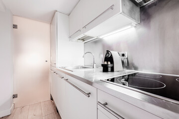 White furniture kitchen with stainless steel countertop and wall covered with stainless steel plate