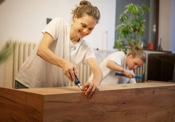 Two young women girlfriends or lesbian couple assembling furniture in their new home. Two women...