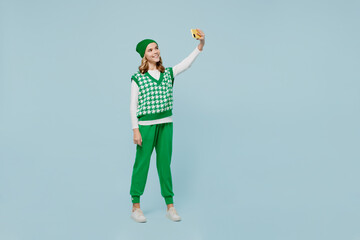Full size body length amazing fun young brunette girl teen student wears checkered green vest hat doing selfie shot on mobile cell phone isolated on plain pastel light blue background studio portrait.