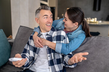 Woman hugging looking at enthusiastic man with remote control