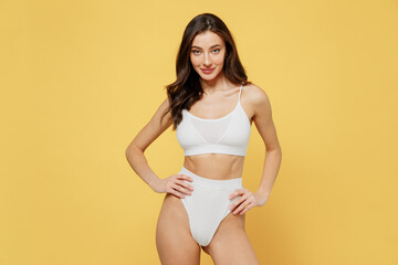 Fototapeta na wymiar Smiling skinny sexy lovely attractive young brunette woman 20s wearing white underwear with beautiful perfect fit body standing akimbo posing looking camera isolated on plain yellow background studio