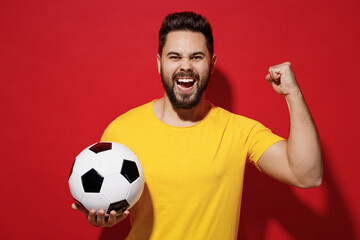 Excited young bearded man football fan in yellow t-shirt cheer up support favorite team hold in...